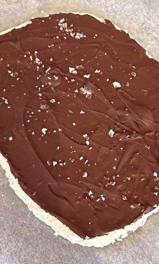 Bitar av fryst bounty bark med kokosbotten, mörk choklad och flingsalt på bakplåtspapper — gjord med POW Vaniljkasein