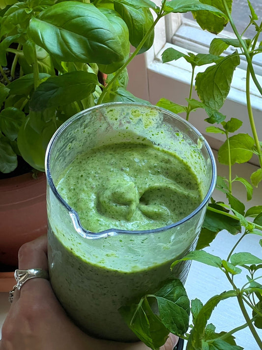 Grön proteinsmoothie med mango, spenat och banan i ett glas, omgiven av gröna krukväxter