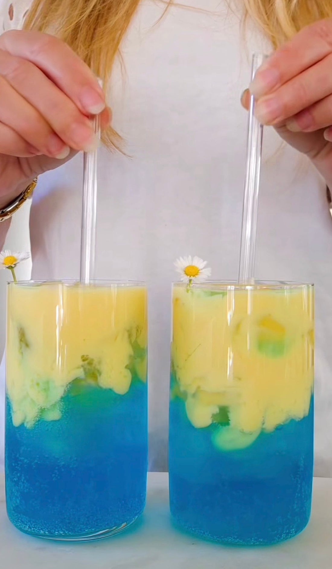 Två blågula glas med dirty soda gjord på POW kaseinprotein vanilj, Vira Blåtira och kokosdryck, toppade med prästkragar och glassugrörsrör