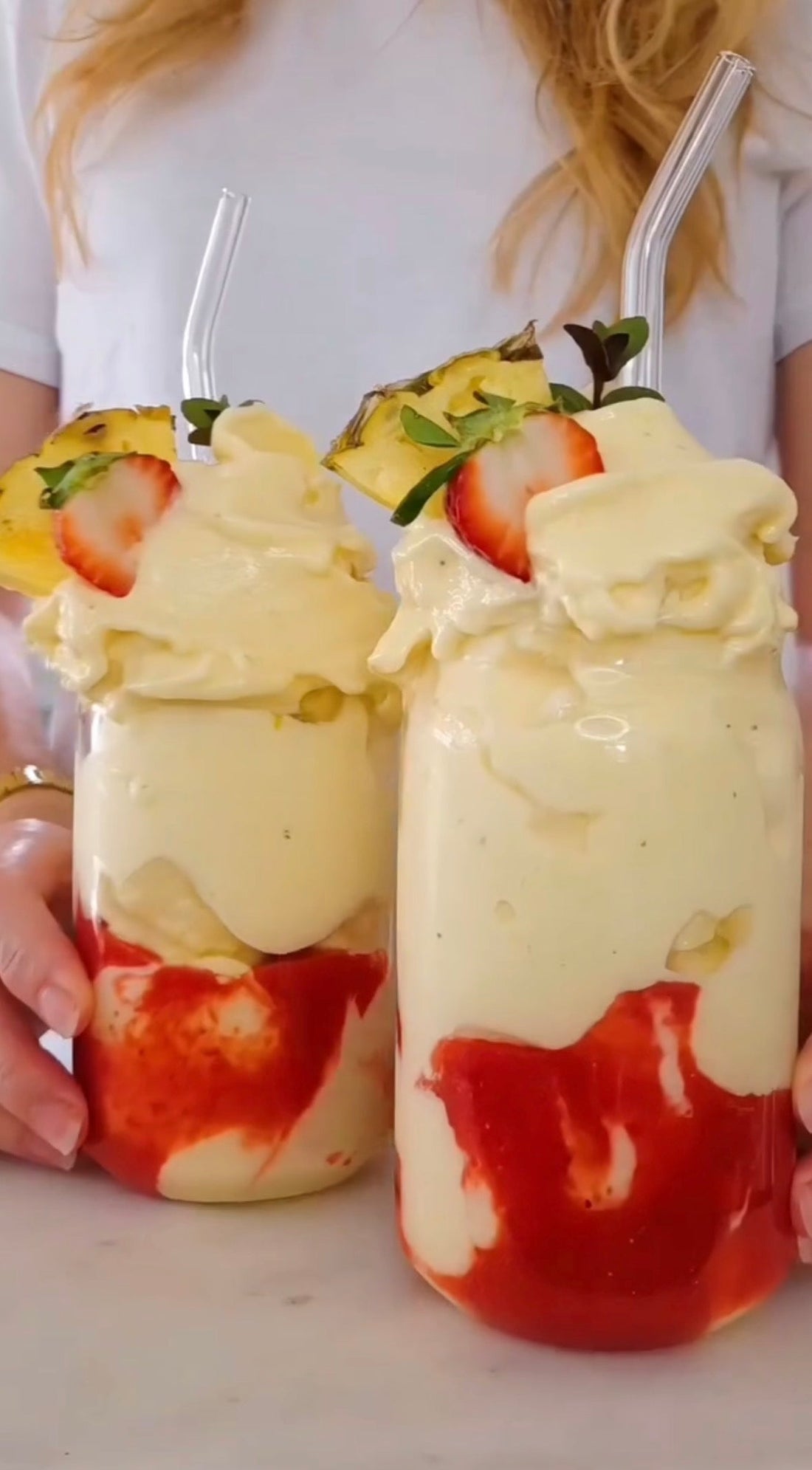 Glas med gul nicecream på en botten av mixade jordgubbar, toppat med ananas och jordgubbe