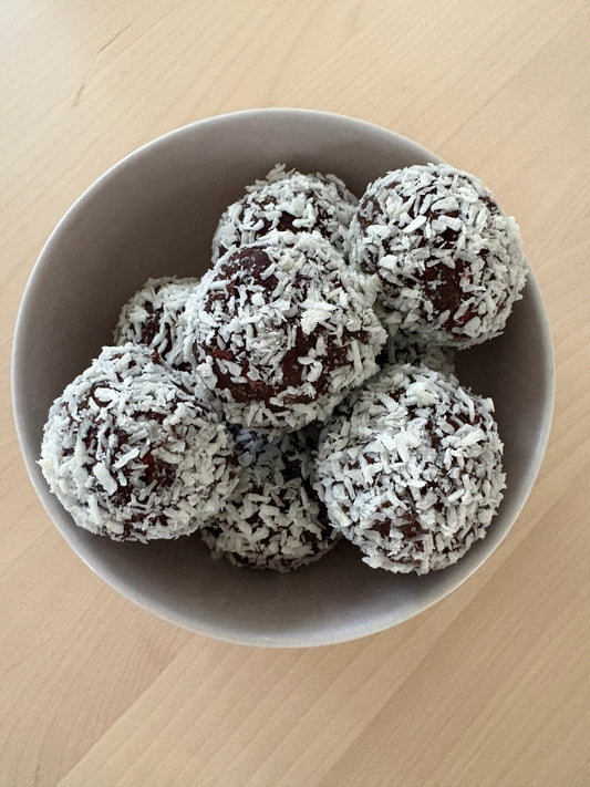 Mintchokladbollar med protein rullade i kokos i en skål, gjorda på dadlar, valnötter och POW kaseinprotein päron & mintchoklad