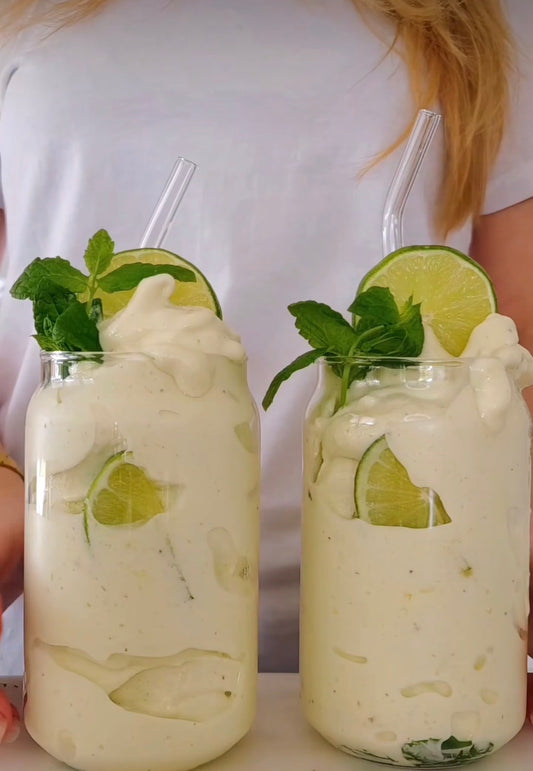 Två glas med mojito nicecream i grön nyans, garnerade med limeskivor och myntakvistar, fotograferade ovanifrån mot ljus bakgrund.