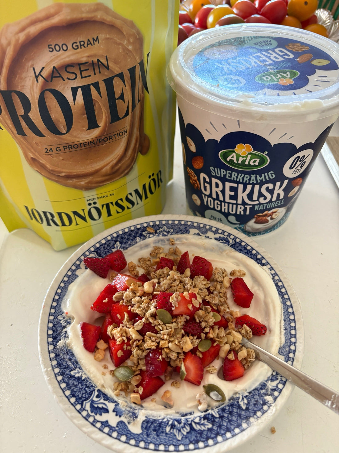 Grekisk yoghurt med kaseinprotein jordnötssmör i blåvit skål, toppad med jordgubbar och granola