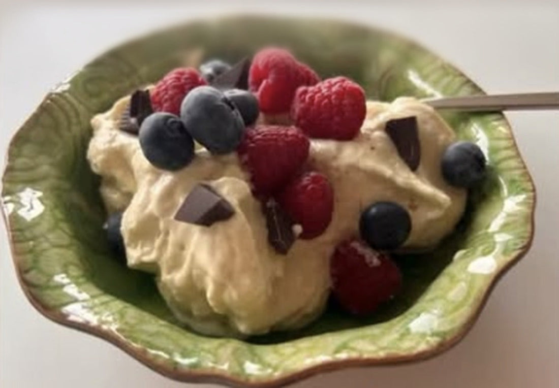 Grön skål med krämig nicecream på kaseinprotein vanilj och mango, toppad med hallon, blåbär och mörk choklad
