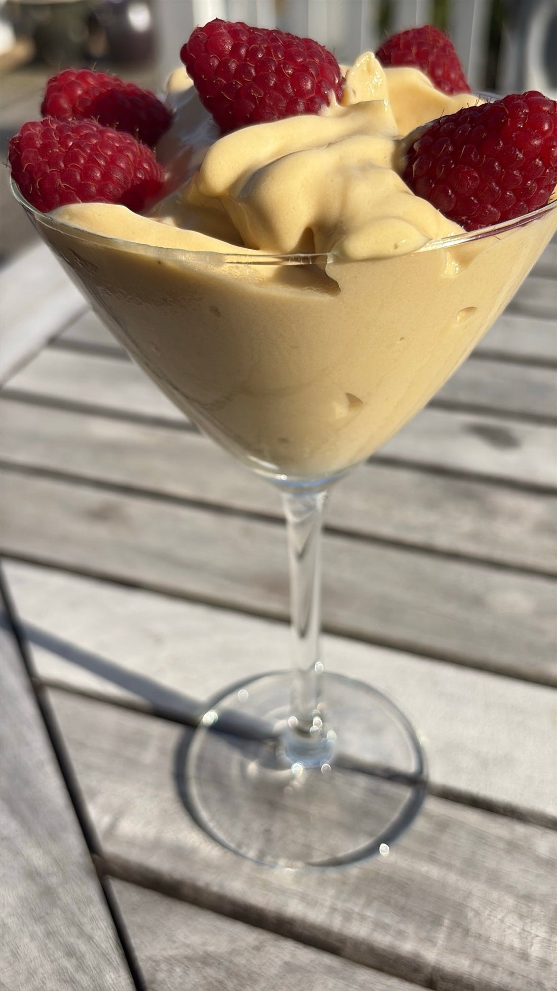 Proteinnicecream med kaseinprotein jordnötssmör, mango och banan i ett martiniglas, toppad med färska hallon