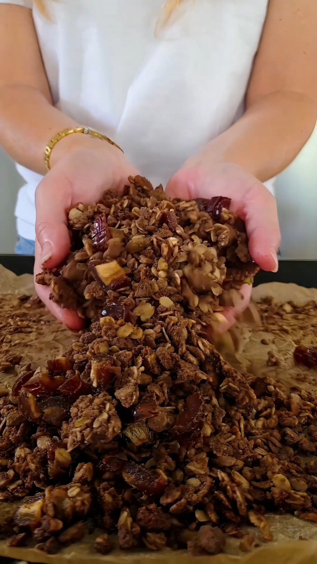 Händer som håller krispig proteingranola med veganskt protein choklad, pistage och medjooldadlar över en bakplåt