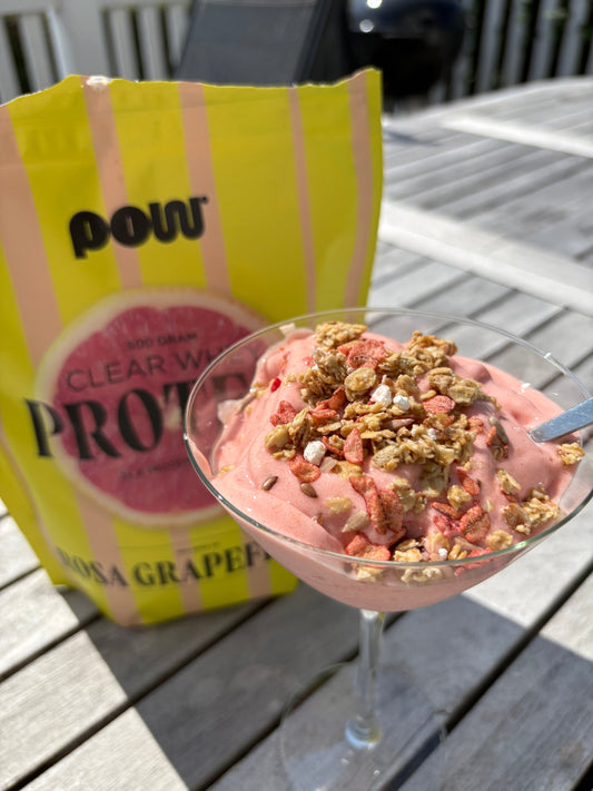 Rosa himmel-proteinsmoothie i glas toppad med granola, bredvid en påse POW Clear Whey Protein