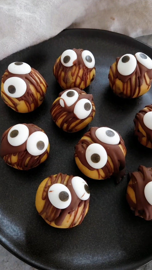 Spooky kakdegsbollar med chokladringel och googly eyes på ett svart fat – proteinbollar med POW kaseinprotein vanilj till Halloween