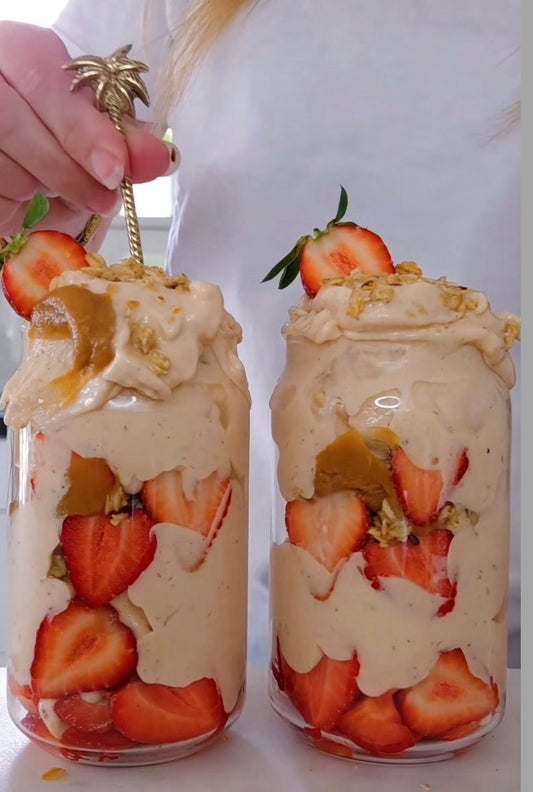 Tjock rosa protein nicecream i glas toppat med färska jordgubbar, granola och kolasås
