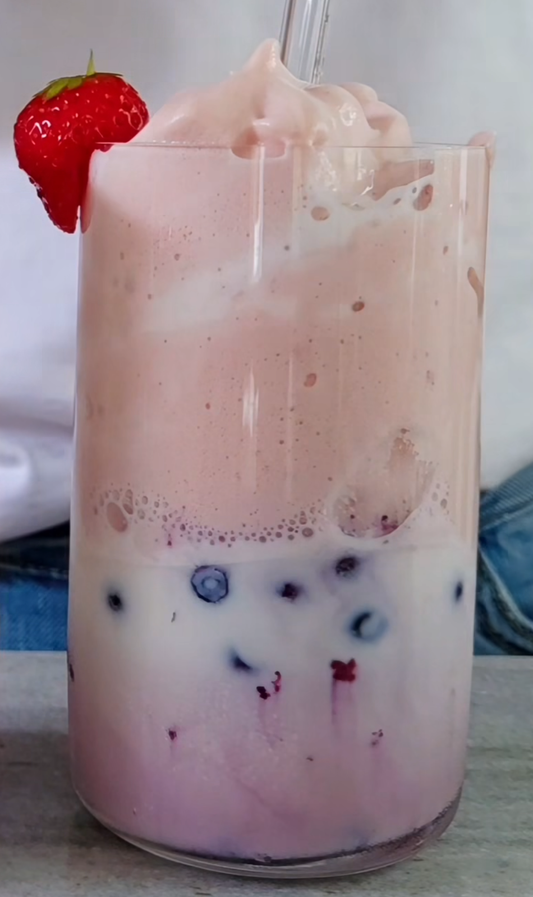 Fluffig rosa proteinmilkshake med blåbär och jordnötssmörskasein, garnerad med jordgubbe
